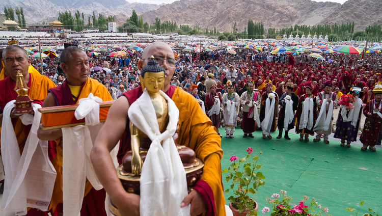 Các thành viên của cộng đồng mang các phẩm vật cúng dường đi ngang qua trước Thánh Đức Đạt Lai Lạt Ma, trong khi các nghệ sỹ địa phương đang biểu diễn bên dưới trong buổi lễ Cúng dường Trường Thọ ở Leh, Ladakh, J & K, Ấn Độ vào ngày 30 tháng 7 năm 2017. Ảnh của Tenzin Choejor / VPĐLLM