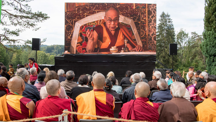 Các thành viên của đám đông quan sát Thánh Đức Đạt Lai Lạt Ma trên một màn hình lớn bên ngoài Chánh Điện trong buổi lễ kỷ niệm lần thứ 50 của Viện Rikon tại Rikon, Thụy Sĩ vào 21 tháng 9, 2018. Ảnh của Manuel Bauer