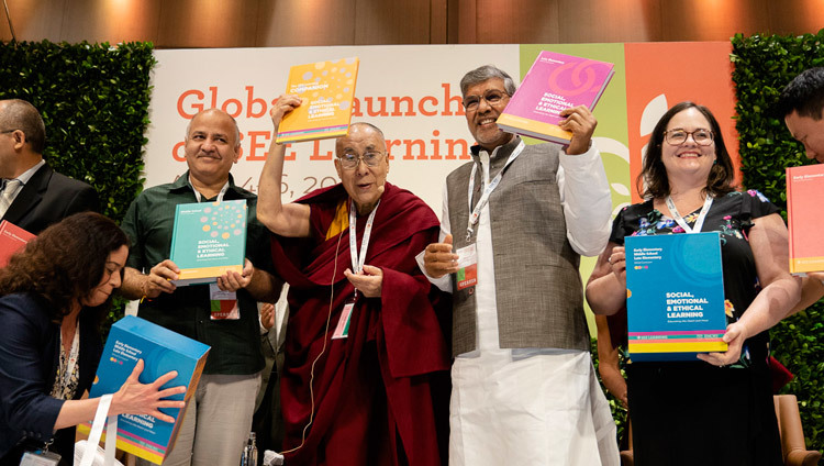 Thánh Đức Đạt Lai Lạt Ma cùng Phó Tổng trưởng Delhi - Manish Sisodia và người được trao giải Nobel Hòa bình -Kailash Satyarthi đang cầm cuốn sách giáo khoa của Chương trình Học tập Cảm xúc và Đạo đức Xã hội tại New Delhi, Ấn Độ vào 5 tháng 4, 2019. Ảnh của Tenzin Choejor