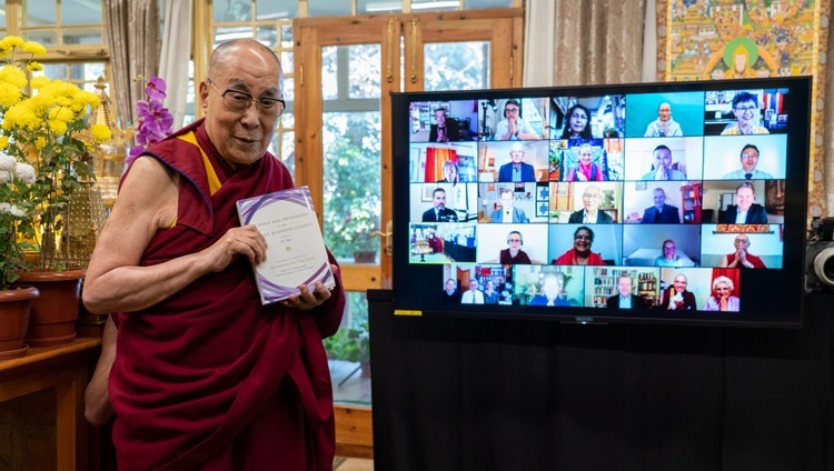 Ngài cầm một bản sao của "Khoa học và Triết học trong Kinh điển Phật giáo Ấn Độ, Tập 2 - Tâm thức” khi Ngài đứng trước TV có hiển thị khuôn mặt của những người đóng góp khác nhau tại Dinh thự của Ngài ở Dharamsala, HP, Ấn Độ vào ngày 13 tháng 11, 2020. Ảnh của Thượng toạ Tenzin Jamphel